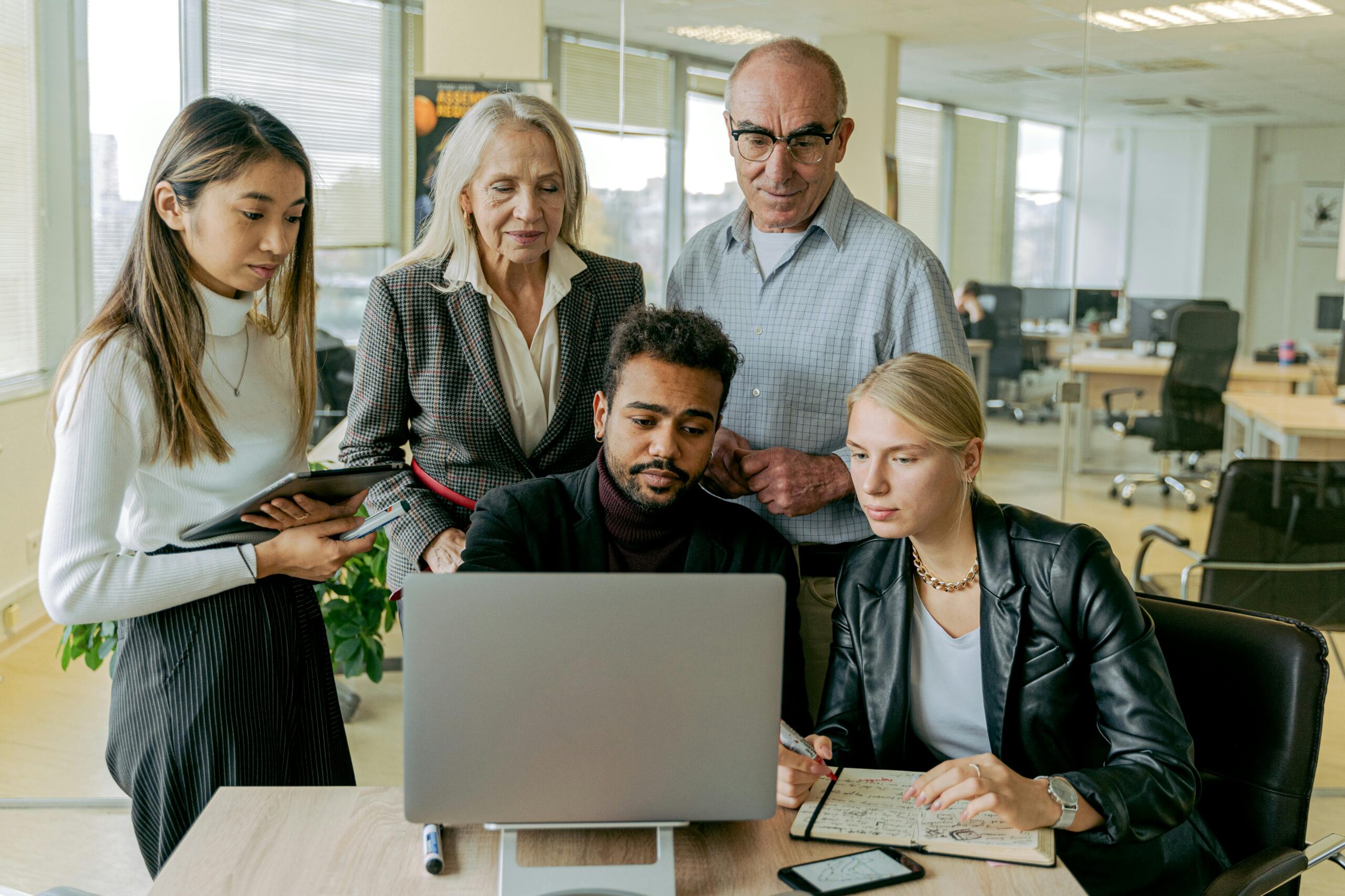 A diverse group of professionals collaborating around a laptop in a modern office setting.